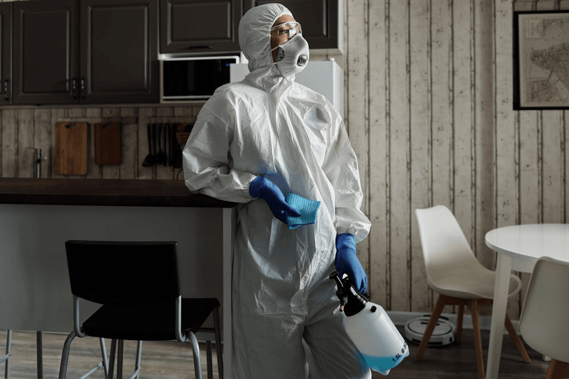 Free Cleaner in PPE suit using a sprayer for disinfection indoors.